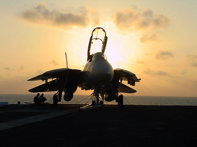 F-14 Tomcat with its canopy raised on an aircraft carrier flight deck at sunset